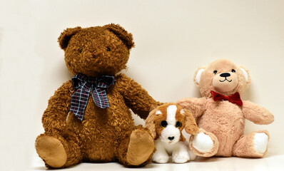 Stuffed brown bear,tan bear and a brown and white dog in the middle of the bears with their paws around the dog,with a red bow tie and a plaid bow tie