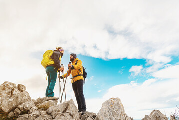 couple of hikers equipped with backpacks and trekking poles look at each other after reaching the top of a mountain. outdoor sports and healthy lifestyle.