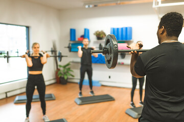 group people lifting weight over their heads looking focused, working out in a gym with other people