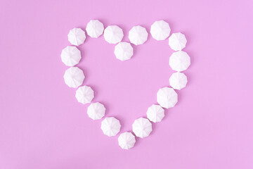 A heart formed by white meringues on a pink background, top down view.
