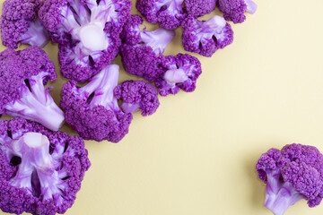 Purple cauliflower florets on yellow background, top view.