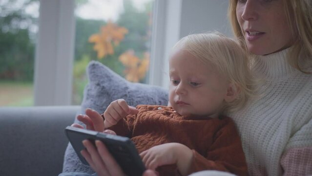 Mother with son sitting at home on sofa playing with smart meter during cost of living energy crisis - shot in slow motion