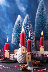 Lovely red and blue advent  Christmas composition. Red burning candles,  wild blue berries and blue decorative trees against blue  textured background. Scandinavian minimalistic style. Still life
