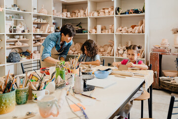 Mature female teacher working with group of kids in pottery workshop