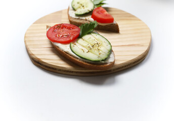 on a wooden kitchen stand are two black bread sandwiches with melted cheese, red tomatoes and green ripe cucumbers and fragrant seasoning and pieces of herbs
