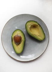 a ripe green avocado with a brown pit lies on a gray kitchen round plate. for banners, labels, shop signs, books with recipes