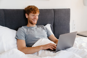 Young handsome smiling redhead man in t-shirt working with laptop