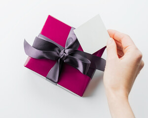 violet gift box with a satin ribbon on a white background. hand puts the card under the gift ribbon