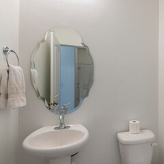 Square White powder room interior with shaped mirror and pedestal sink
