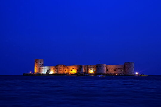 A castle in the middle of the sea, illuminated at night in the blue hour. Mersin kız kalesi