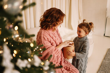 A little daughter, a child and a pregnant mother in knitted sweaters cuddle spend time together in the decorated interior of a Scandinavian-style room on a Christmas holiday at home. Selective focus