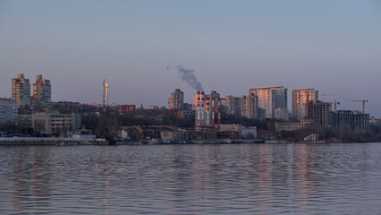 View of the city from the water. Smoke comes from chimneys.