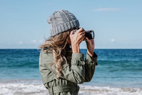 Young woman photographing seascape on beach