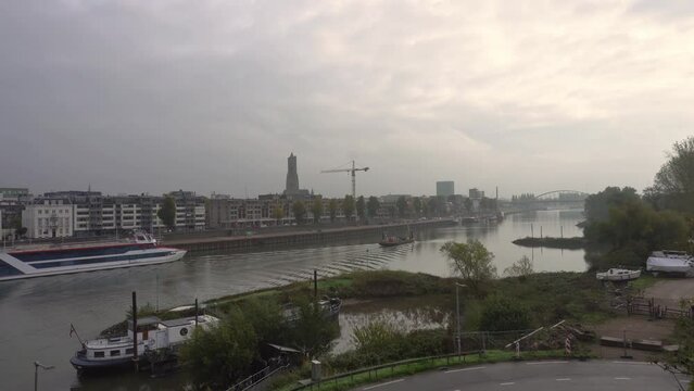 Skyline of the Dutch city Arnhem with boats in front seen from the bridge over the river Rhine on an overcast day
