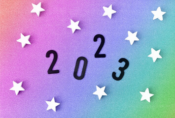 2023. New Year's Eve Card. Black 2023 and White Wooden Stars Sprinkled on a Rainbow Brocade Background. Funny Carnival Flatlay Composition ideal for Card, Greetings Banner, Newsletter. 