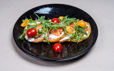 Close-up of fresh potato pancakes with arugula, cherry tomatoes and salmon on a beautiful black plate. Delicious food in the restaurant.