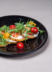 Close-up of fresh potato pancakes with arugula, cherry tomatoes and salmon on a beautiful black plate. Delicious food in the restaurant.