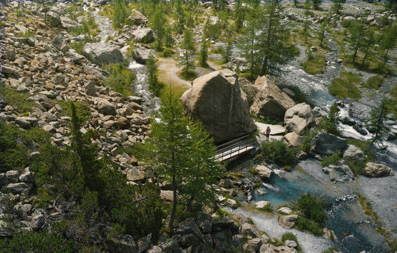 Aerial view of one person who's about to cross a bridge over a stream while trekking in the beautiful landscape of the Alpe Ventina in Chiesa in Valmalenco, Lombardy, Italy.