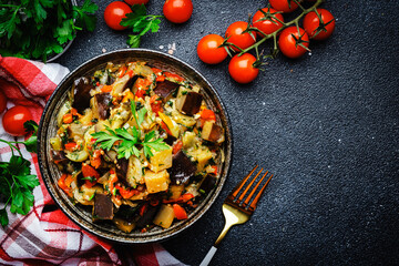 Vegetable stew, saute or caponata. Stewed eggplant with paprika, tomatoes, herbs and spices. Black kitchen table background, top view, copy space