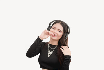 Fototapeta premium A female teenager jams with the beat of the music with her black wireless headphones while eating lollipop in a studio with white background.