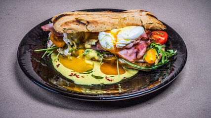 Delicious freshly prepared breakfast on black plate. Fried eggs on bacon. Toasted bread. Cherry tomatoes, arugula.
