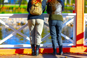 Rear view of female friends standing together in the park at sunset or sunrise in the warm rays of the sun near the pond. Concept of women meeting for communication