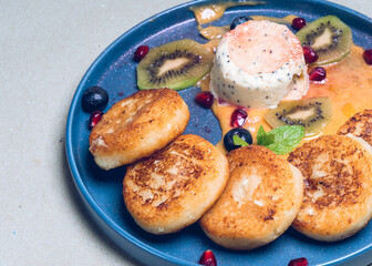Freshly prepared food. Delicious dessert. Cheesecake pancakes with fruits, berries and sweet sauce on beautiful blue plate. Close-up.