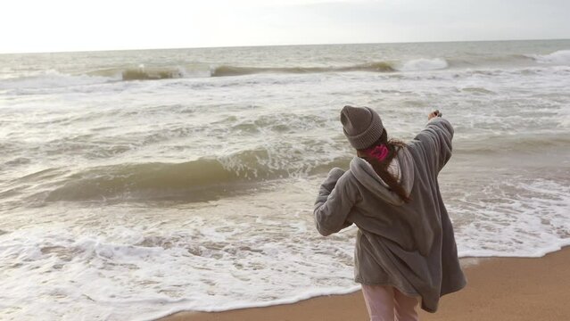 Woman is filming or photographing the stormy seas from the beach with a cell phone.