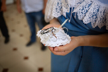 A golden cross on a small white pillow in the hands of a godmother in an Orthodox church