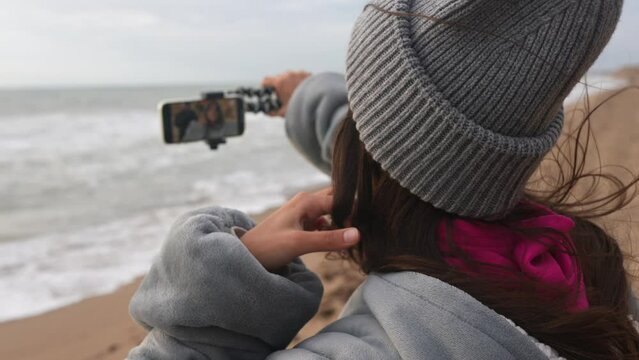 Woman is filming or photographing the stormy seas from the beach with a cell phone.