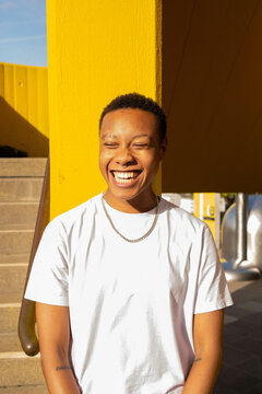 Portrait of a young black trans man smiling in the sun.