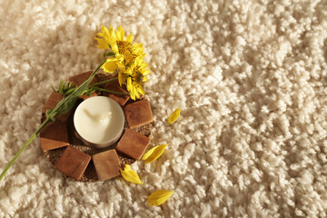 Fototapeta na wymiar an aroma candle on a wooden stand and a yellow autumn flower on a milk-colored carpet. cozy atmosphere.
