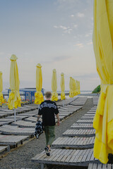 the guy walks forward along the beach along the yellow umbrellas and deck chairs