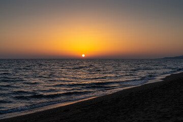 Fototapeta premium sunset on the Mediterranean Sea in Greece with calm ocean water and dark sand beach in the foreground