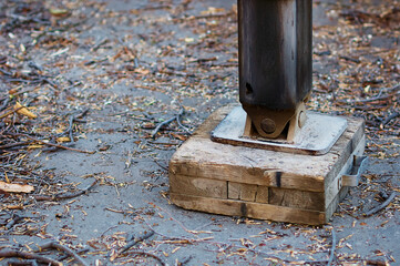 The hydraulic outrigger of the telescopic truck tower is mounted on a wooden portable platform. Work on sanitary pruning of trees in the park. Fragments of branches and bark on the ground. Close up.