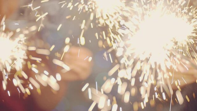 Closeup of hands lighting sparklers. Multiracial young people celebrate New YEAR XMAS, smile and laugh. Merry Christmas winter holiday concept. Friends spend time together. Festive emotional mood