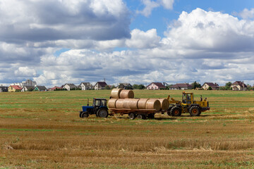 Obraz premium A tractor loading round hay bales on to a trailer