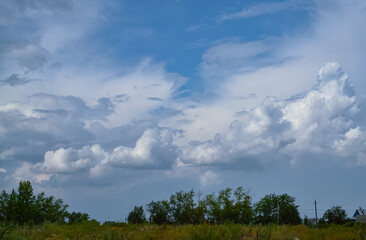 Obraz premium Beautiful sky and white cumulus clouds on it over trees and a field with green grass