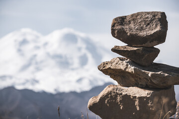 The stones stand on top of each other in a pyramid against the backdrop of Mount Elbrus, a cloudy autumn day in the Caucasus