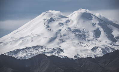 Fototapeta na wymiar Two peaks of Mount Elbrus in the Caucasus with side illumination and clouds on the peaks, snow and glaciers with cracks on the peaks close up