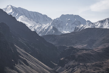 Alpine rocky valley without vegetation on the background of a mountain range with snow and glaciers, monochrome mountain landscape