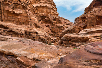 Typical landscape at Petra, Jordan, rocky walls around, few small green plants growing in red dusty...