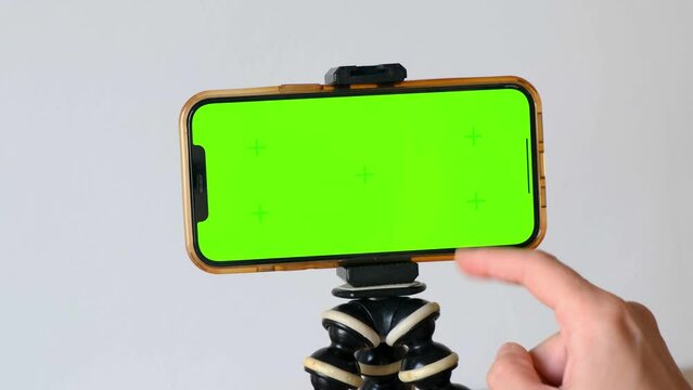 Finger swipes left green screen of smartphone, horizontally on tripod on white background, viewing chromatic key online, reading social networks, news