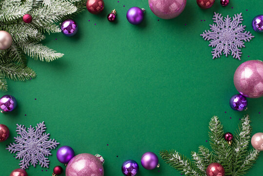 Christmas concept. Top view photo of violet and pink baubles snowflake ornaments fir branches in snow and purple sequins on isolated green background with blank space in the middle