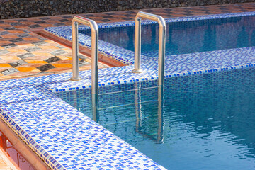 A metal swimming pool safe ladder (skimmer) on the entrance to the home inground poolside with the...