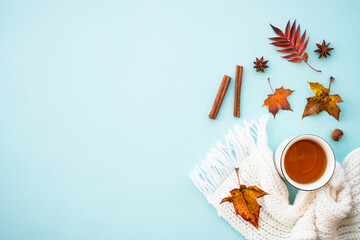 Autumn background on blue. Hot tea, knitted scarf and fall leaves. Flat lay composition with copy...