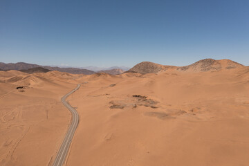 Fototapeta na wymiar Aerial photo of a road in the atacama desert with a blue sky and mountains behind
