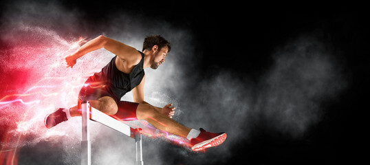Man athlete at hurdle race, jumping over the last hurdle - 541797222