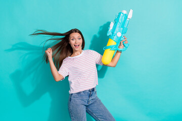 Photo of ecstatic impressed woman with straight hairstyle wear striped t-shirt hold water gun clench fist isolated on teal color background