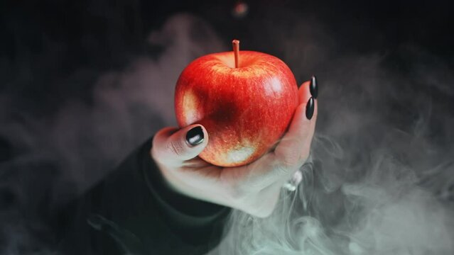 Woman as witch offers red apple as symbol of temptation, poison. Fairy tale, white snow wizard concept. Spooky halloween, cosplay. Smoke, haze background.